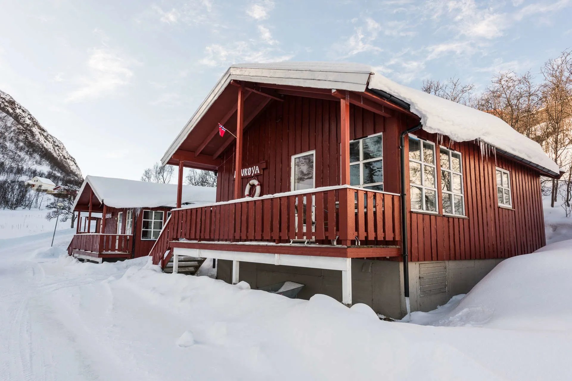 Red cabin with a covered porch by a blue bay on a sunny day.