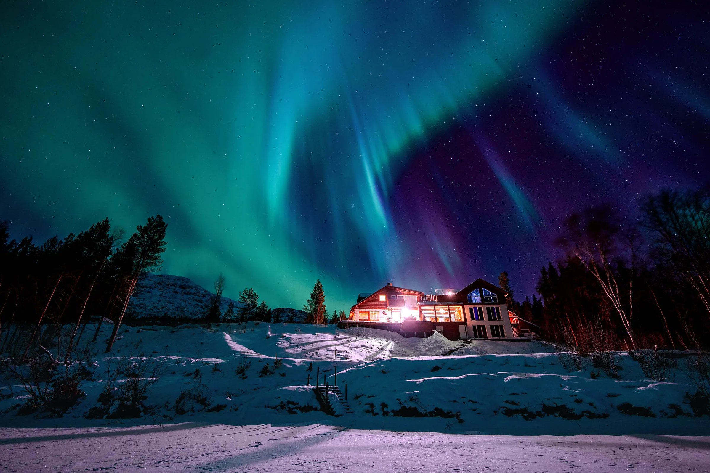 Aerial view of Reisa Lodge in winter with a hot tub on the deck, surrounded by snow.