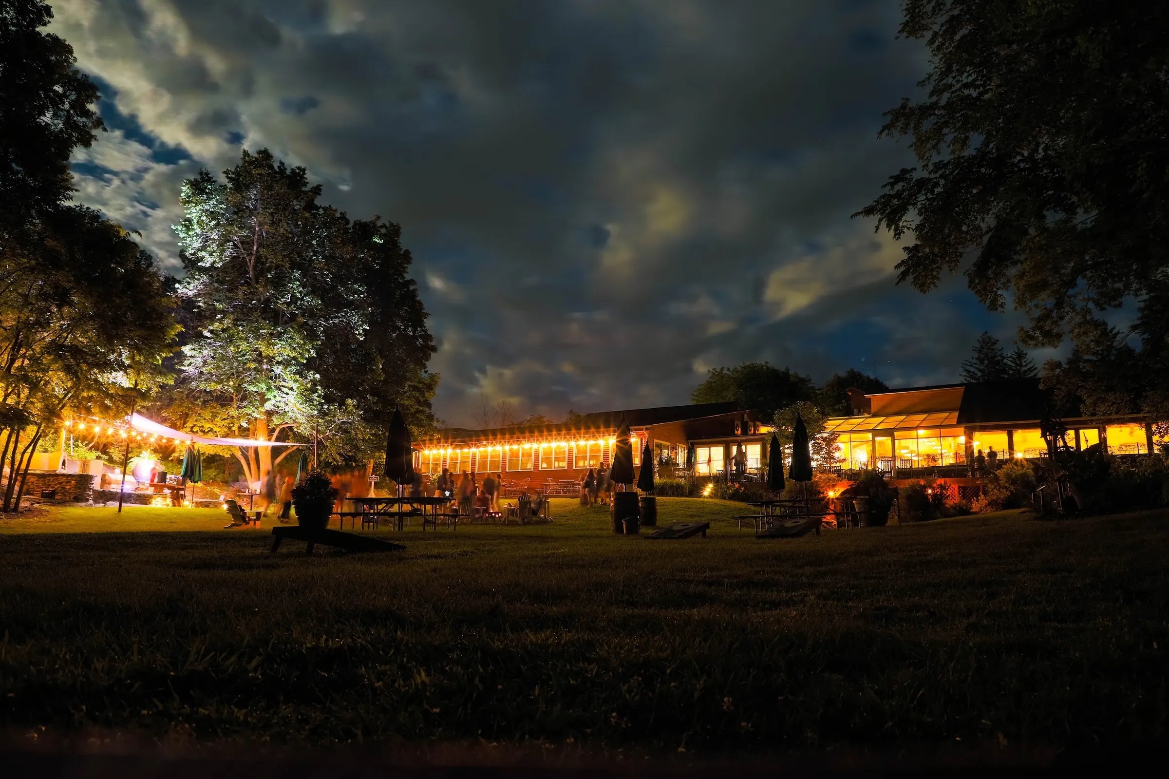 Main lodge building illuminated at night with outdoor string lights and guests socializing