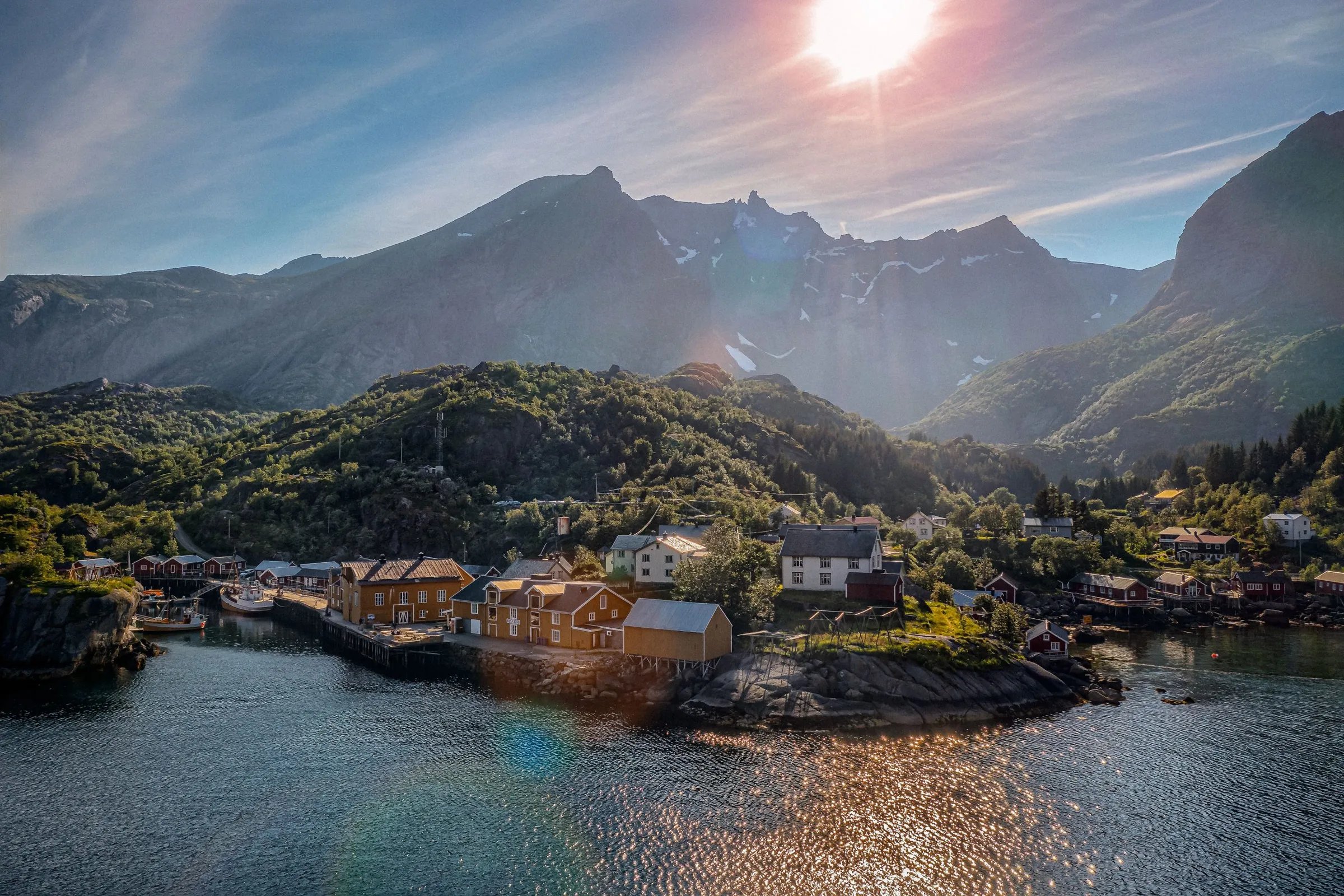 Aerial view of Nusfjord village nestled in a fjord with mountains and sun flare