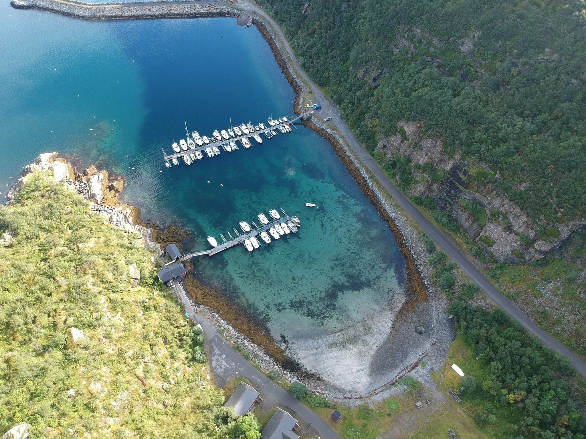 Aerial view of Skjervøy town and harbor nestled among green hills by a blue bay.