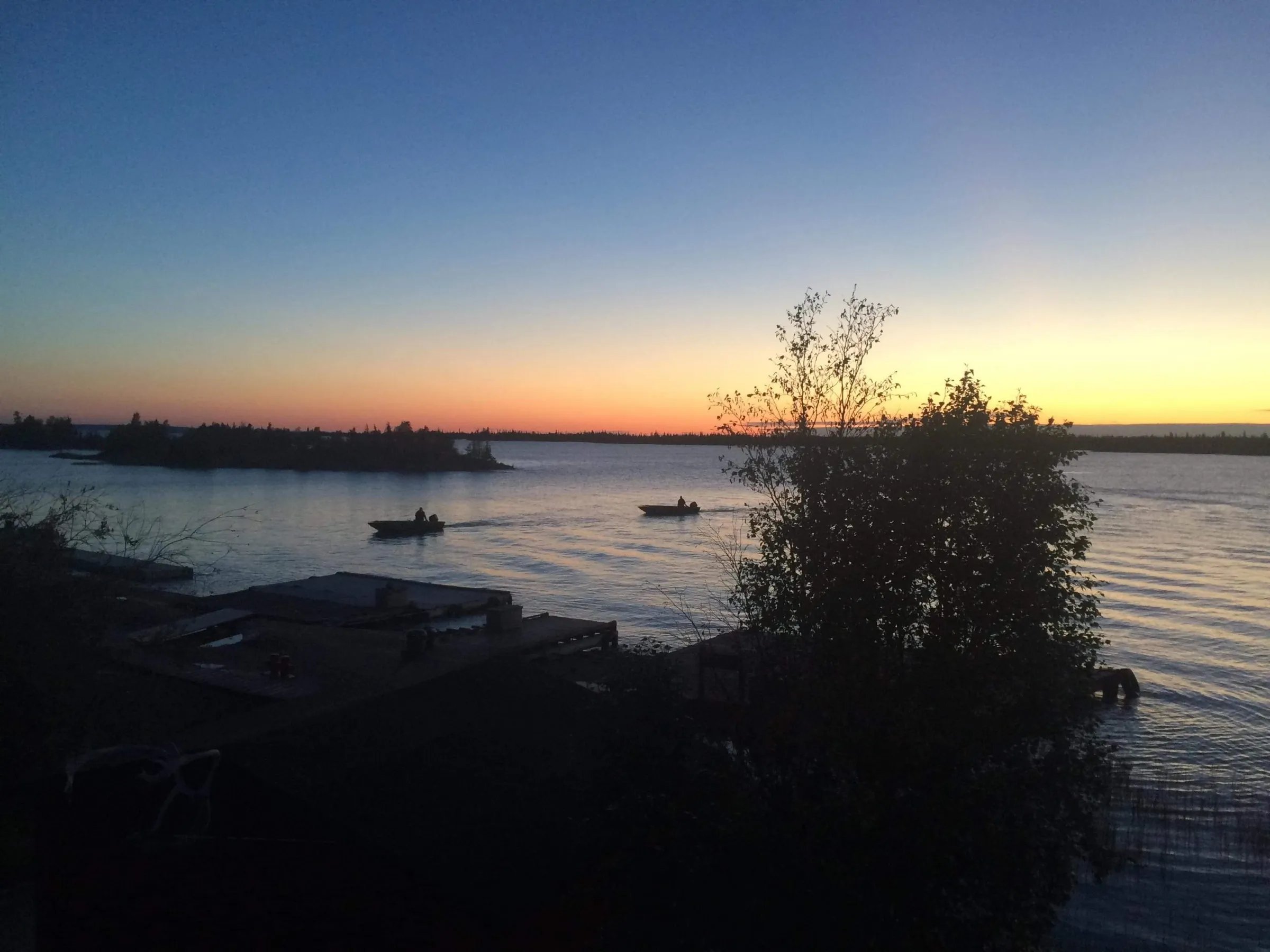 Sunset over a calm lake with two fishing boats on the water.