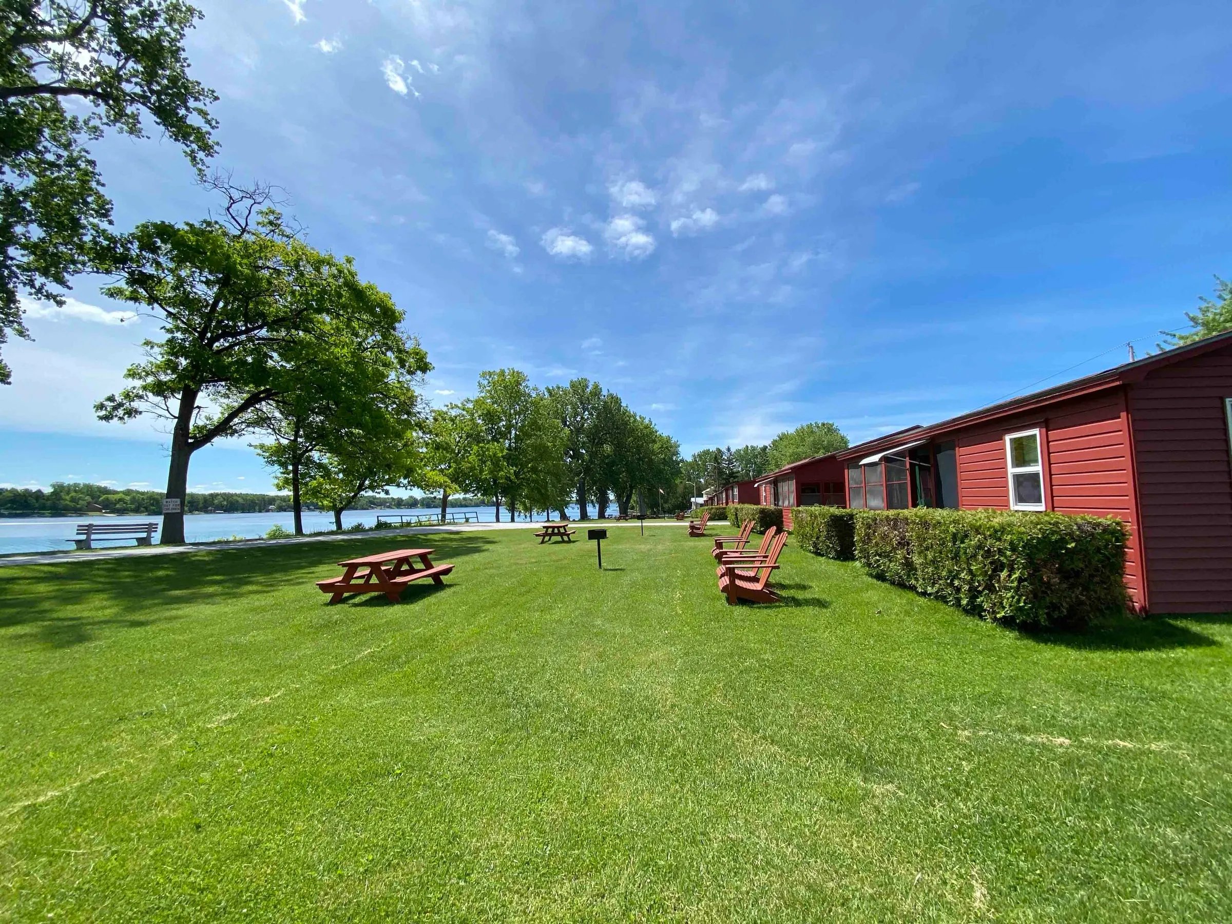 Sunny lawn area with red picnic tables and Adirondack chairs in front of red cottages by the lake