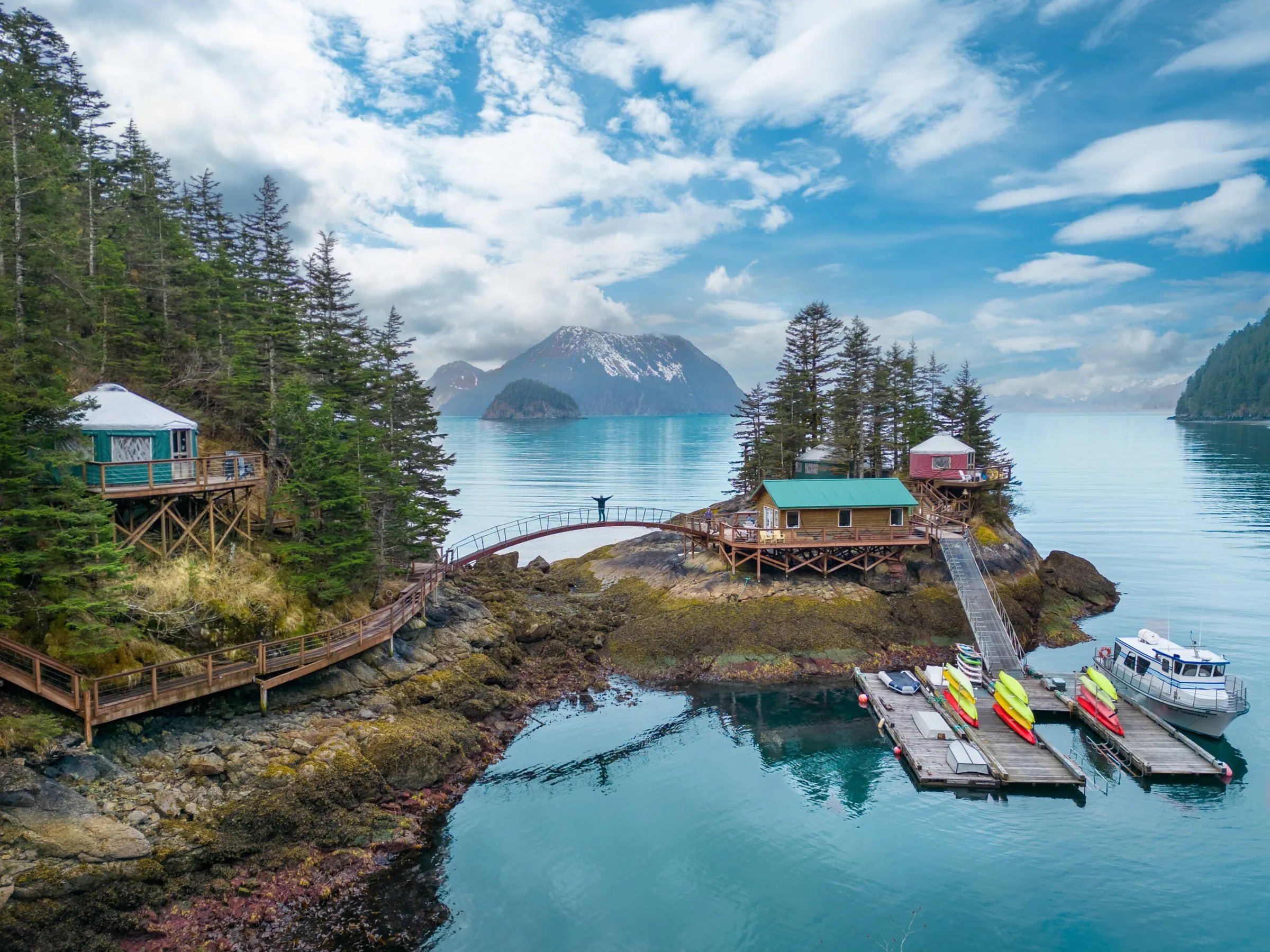 Aerial view of Orca Island Cabins, featuring yurts, main lodge, docks, and surrounding bay with mountains.