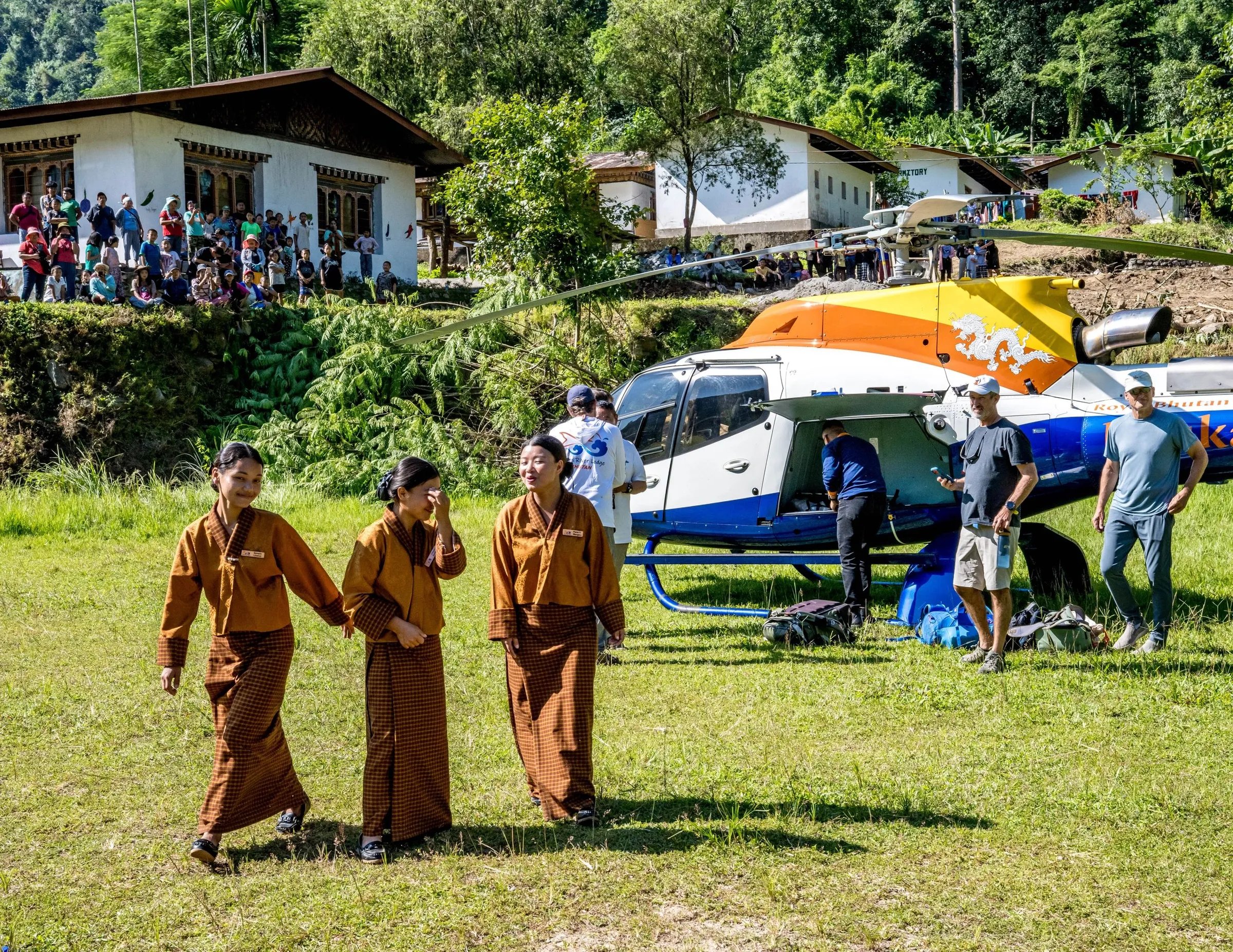 Helicopter on a grassy landing strip with people and lodge buildings in the background