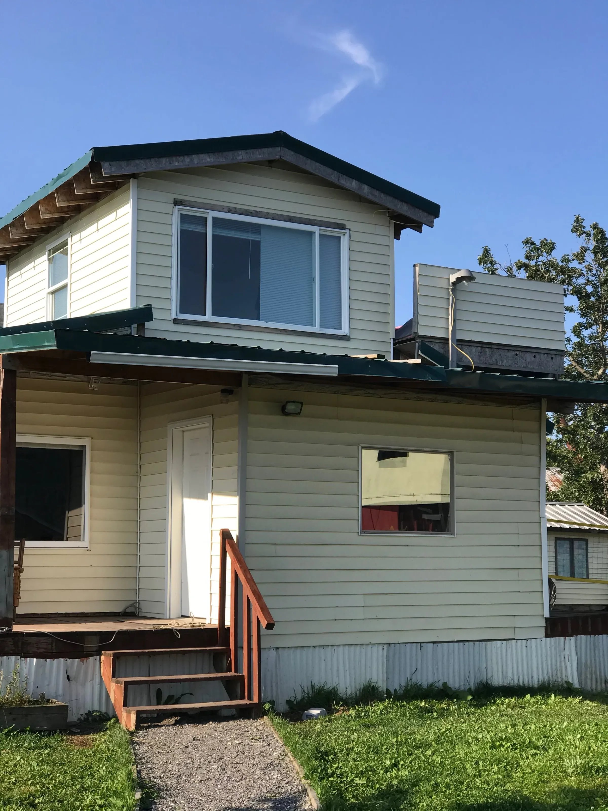 Two-story house with beige siding, green roof, and a small porch