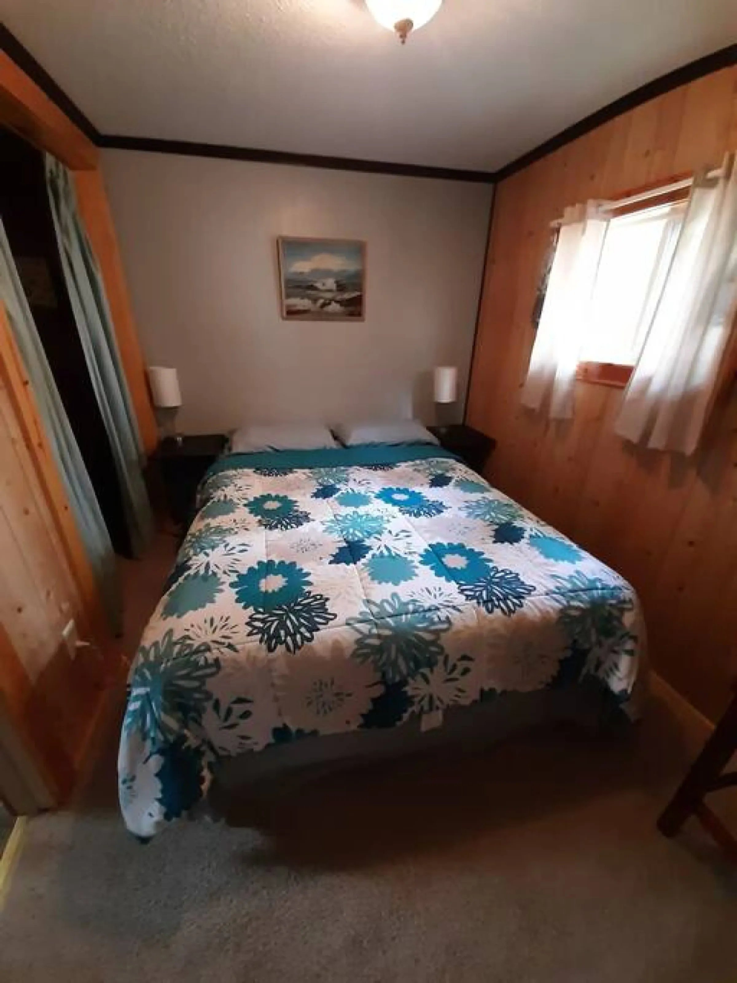 Cozy bedroom with a queen bed, blue floral quilt, and wood-paneled walls