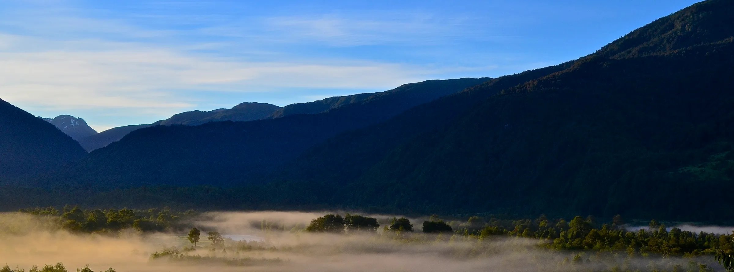 Misty valley at sunrise with dark mountain silhouettes