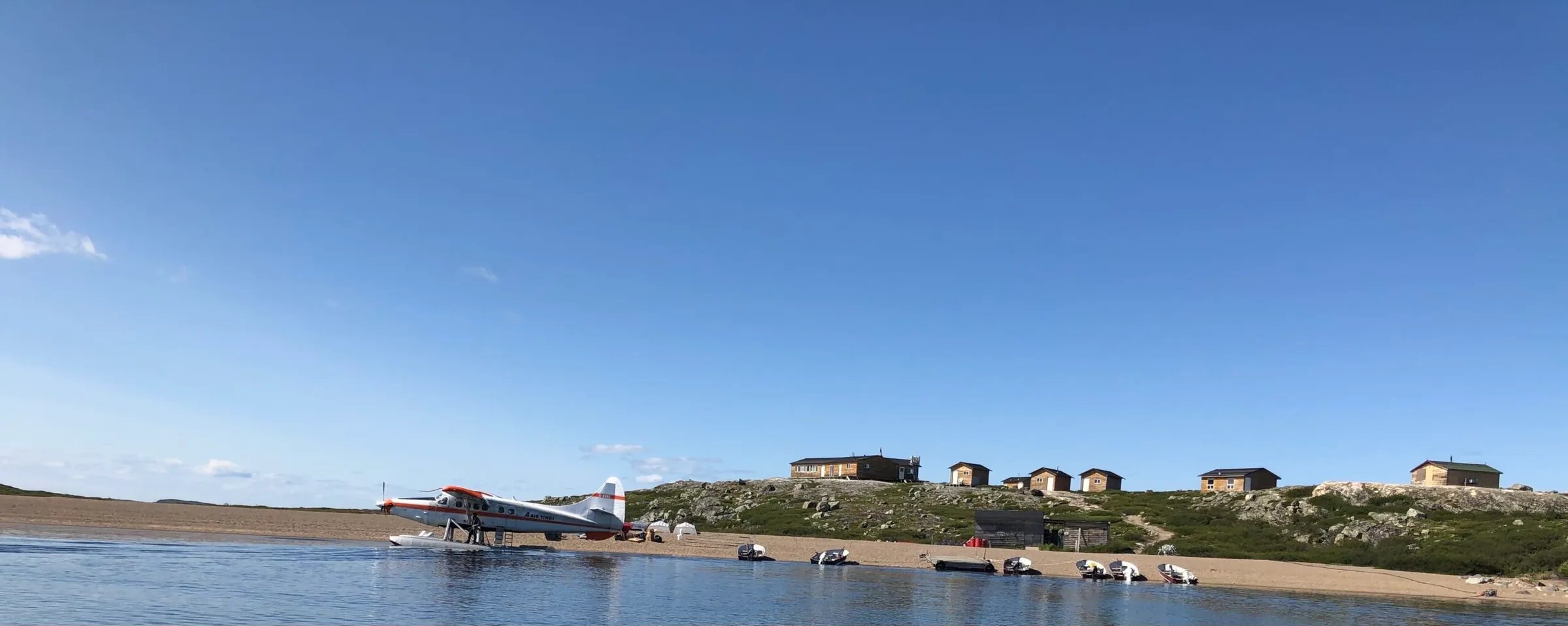Panoramic view of the lodge camp with multiple buildings along a rocky shoreline from the water
