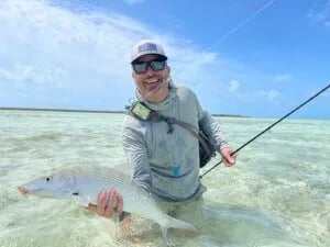 Angler holding a shimmering permit in clear shallow water under a sunny sky