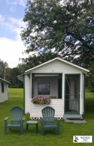 White cabin exterior with a screened porch, flower box, and two green Adirondack chairs