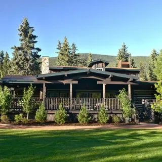 Log lodge building with a wide porch and surrounding pine trees