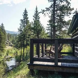 Rustic log cabin deck with Adirondack chairs overlooking a stream