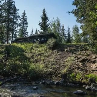 Log cabin nestled on a grassy hill overlooking a winding stream