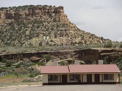 Motel-style building with a red roof against a rocky mesa