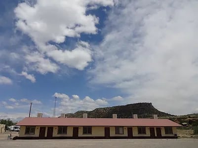 Long motel building with a red roof under a bright blue sky with clouds