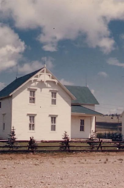 Historic white lodge building with a green roof and decorative gables, behind a wooden fence.
