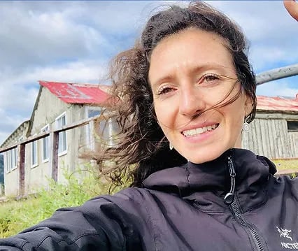 Woman smiling in front of a rustic lodge building with a red roof