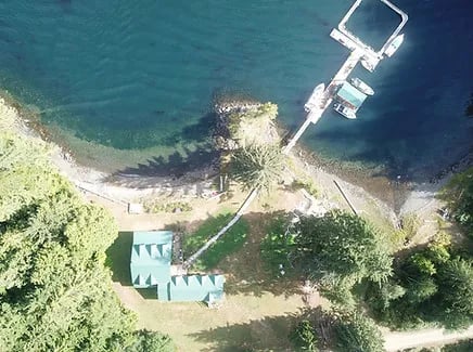 Top-down aerial view of the lodge buildings and a long dock extending into the clear blue water