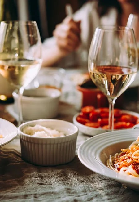 Dining table set with wine glasses, pasta, and side dishes