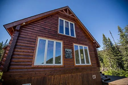Rustic log cabin with multiple windows under a clear blue sky.