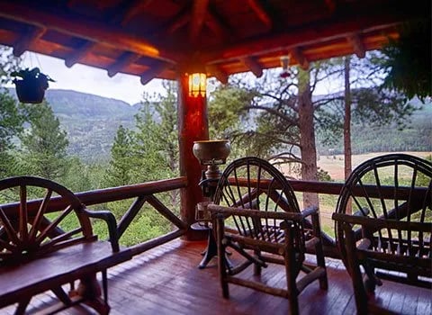 Covered wooden porch of the main lodge with Adirondack chairs and a mountain view