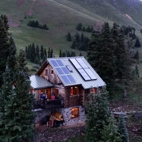 Aerial view of the wooden hut with solar panels on the roof, surrounded by trees.