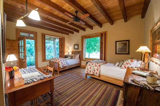 Guest bedroom with two single beds, wood-beamed ceiling, and large windows.