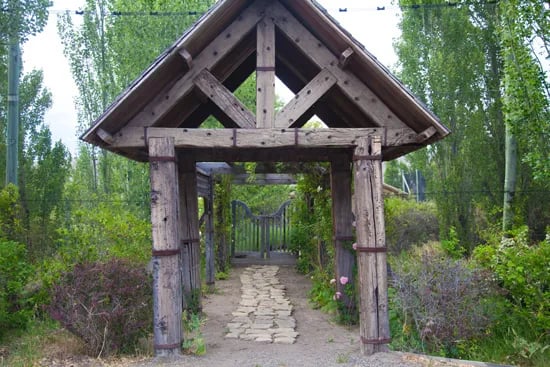 Wooden archway entrance with a stone path leading into a green, wooded area.