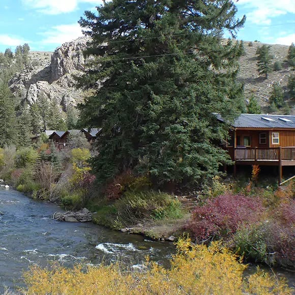 Cabin with a deck overlooking a river, surrounded by autumn foliage