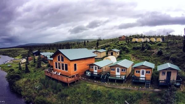 Wooden lodge building with a green roof on a forested hill at sunset