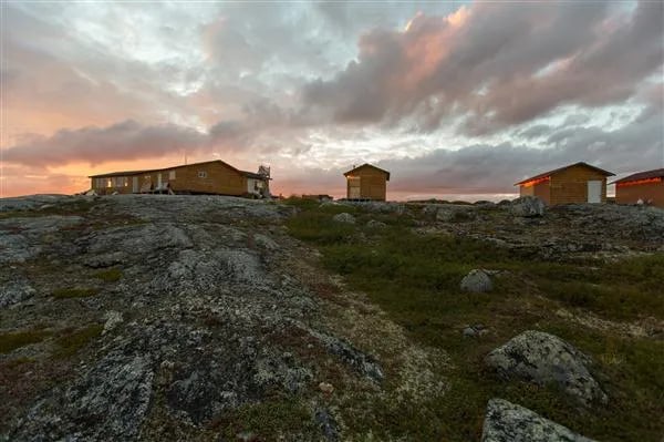Multiple lodge buildings on a rocky hill at sunset with a dramatic cloudy sky