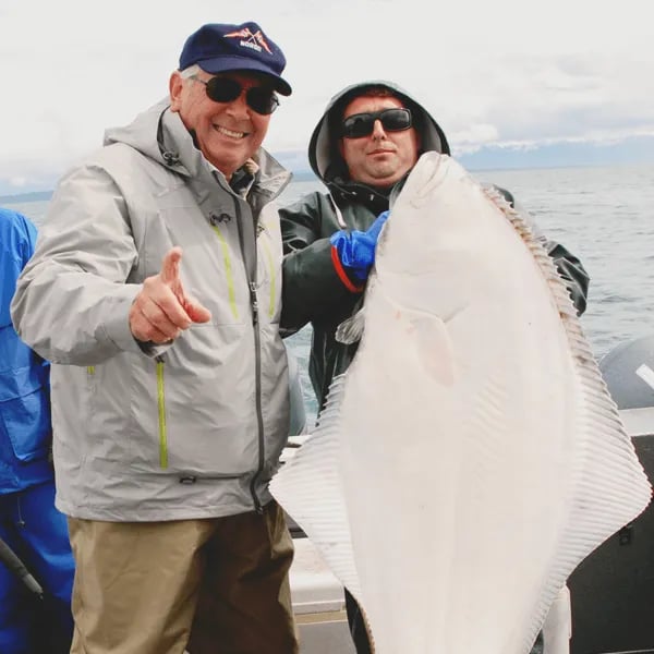 Smiling angler giving a thumbs up next to a large halibut on a boat