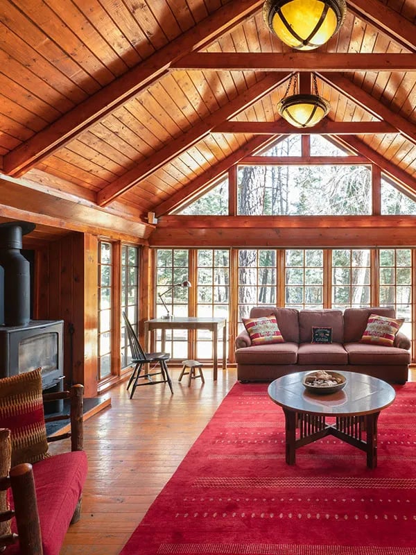 Juniper Cabin living room with a vaulted wood ceiling, red rug, and large windows overlooking the forest.