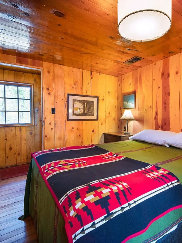 Juniper Cabin bedroom with a colorful native-patterned blanket on the bed and knotty pine walls.
