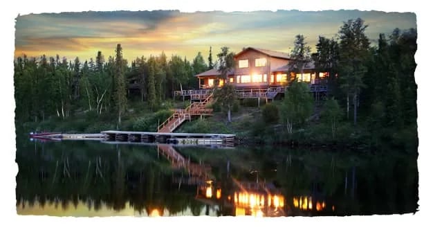 Main lodge building on a lakefront at sunset, lights glowing from windows