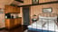 Bedroom with warm wood paneling, a black metal-frame double bed, and a compact kitchenette