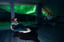 Woman in a cozy sweater watching green Northern Lights from a large window in a lodge room.