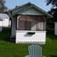 White cabin exterior with a green-trimmed screened porch and an Adirondack chair