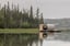 Unique floating barrel cabin with a large round window, surrounded by a calm lake and forest