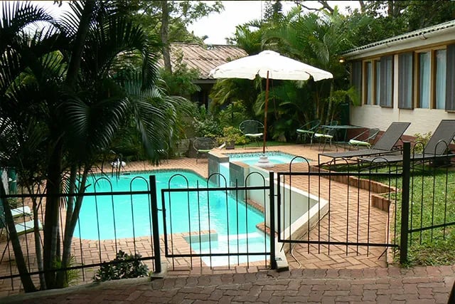 Swimming pool area with sun loungers and a white umbrella, surrounded by lush tropical plants