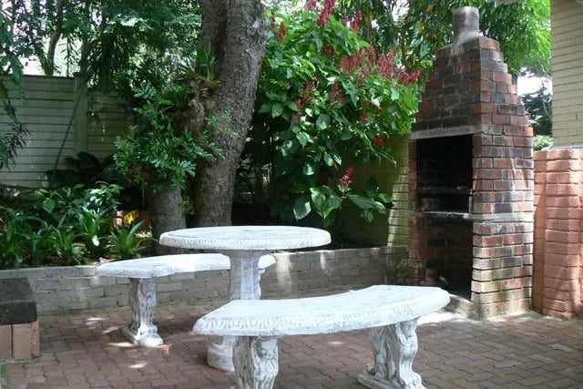 Outdoor braai area with a brick grill and stone table and benches under trees