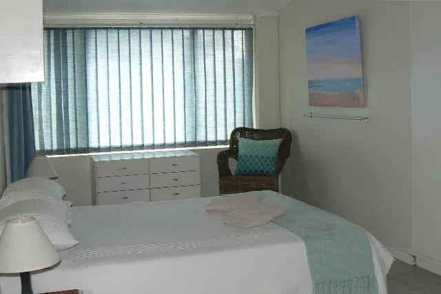 Bedroom with a white bed, blue accents, and vertical blinds on the window