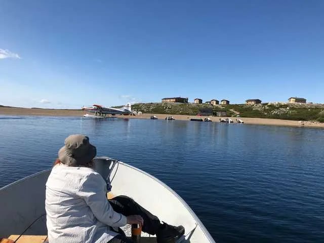 Person in a boat approaching a distant lodge camp on a sunny day