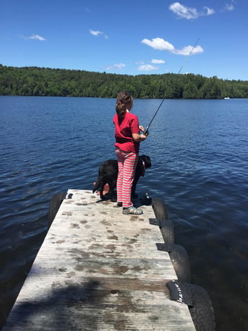Man and child smiling, holding a large fish on a wooden deck.
