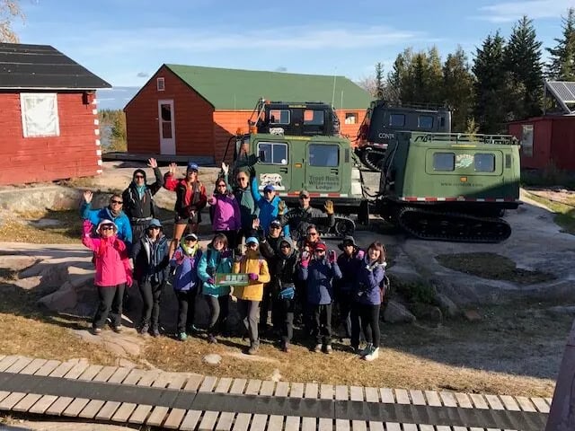 Group of people posing in front of lodge buildings and tracked vehicles.