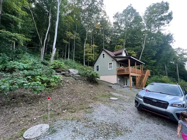 Lodge exterior with a silver SUV parked in the gravel driveway, surrounded by lush trees.