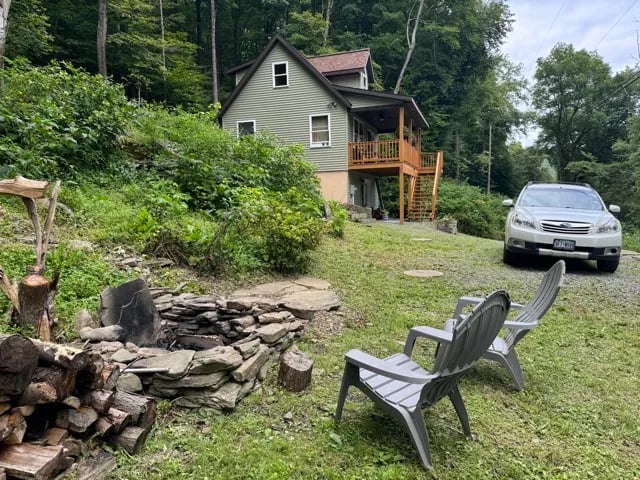 Lodge exterior with a stone fire pit, Adirondack chairs, and a silver SUV in the driveway.