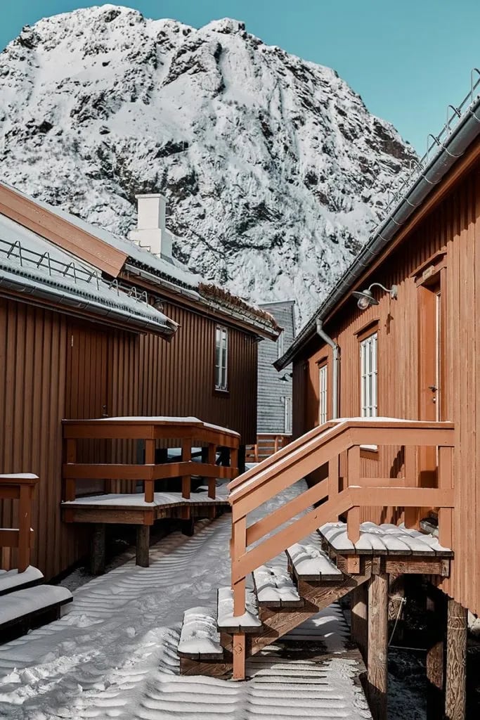 Traditional red rorbuer cabins covered in snow with a large snowy mountain in the background.