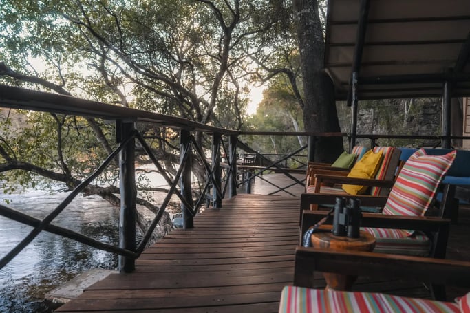 Thatched-roof lodge building with a wooden deck overlooking a sandy area.